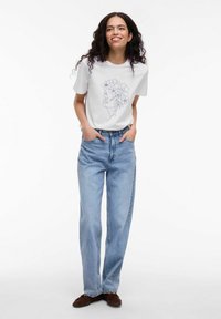Hvid bomulds t-shirt med en linje tegning af et ansigt med blomster. Kombineret med lyseblå højhalsede denim jeans. Brune slip-on sko.