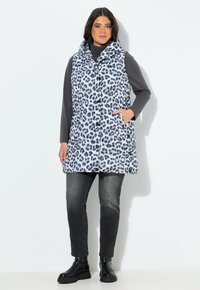 Gilet imbottito in stampa leopardo grigio e nero, dotato di cappuccio, tasche frontali e chiusura con bottoni. Indossato sopra una maglia grigia e jeans scuri.