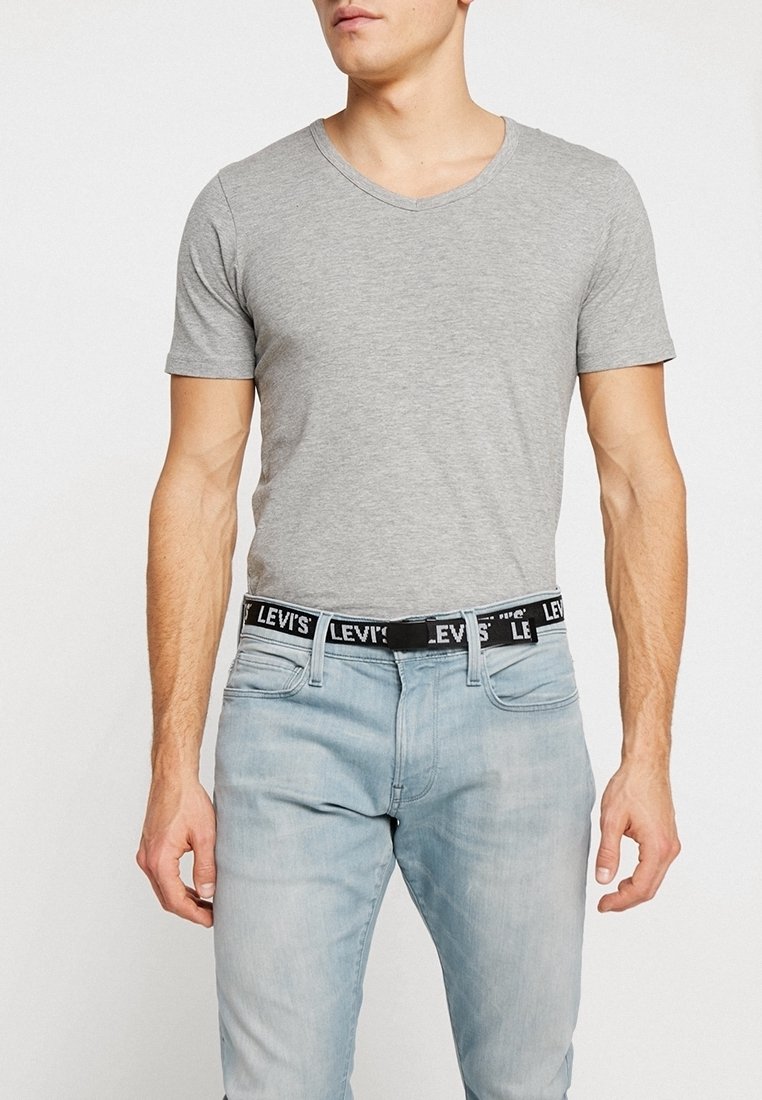 Homme portant un t-shirt ajusté gris clair à manches courtes, un jean bleu clair et une ceinture noire Levi's avec lettrage blanc du logo.