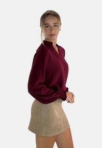 Bordeaux blouse met een hoge kraag, textuurstof en elastische mouwen, gecombineerd met een beige suède minirok.