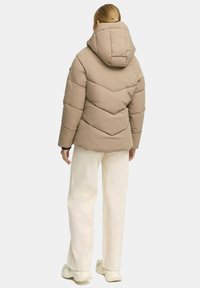Beige pufferjack met een capuchon, met een chevron-gequilt ontwerp. Gecombineerd met romige wijde broek en lichte sneakers.