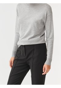 Maglione grigio lavorato a maglia con un elevato collo, polsini a coste e una vestibilità rilassata, abbinato a pantaloni neri sartoriali con pieghe frontali.