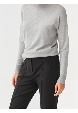 Grau gestrickter Pullover mit einem hohen Kragen, gerippten Bündchen und einem lockeren Schnitt, kombiniert mit taillierten schwarzen Hosen mit Bundfalten.
