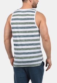 Ermeløs striped tank topp med blå og grønne horisontale striper på en hvit bakgrunn, laget av et mykt og teksturert stoff.