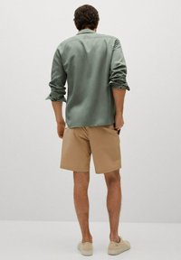 Lichtgroen shirt met lange mouwen en opgerolde manchetten, gecombineerd met beige shorts. Simpel ontwerp, zachte textuur en neutrale kleuren.
