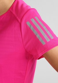 Camiseta deportiva rosa de manga corta, con un patrón texturizado y tres franjas reflectantes en el hombro izquierdo.