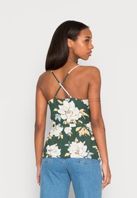 Top peplum floral em verde escuro com flores brancas e amarelas, apresentando alças finas, cintura ajustada e um tecido texturizado.