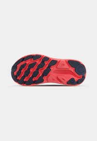 Semelle de chaussure de sport rouge et noire avec des motifs texturés et des crampons prononcés pour une adhérence et une stabilité sur diverses surfaces.