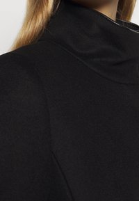 Black coat featuring a high collar, smooth texture, and clean lines. The fabric appears soft, with a minimalist design and no visible hardware.