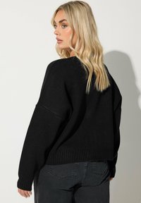 Svart stickad tröja med avslappnad passform, ribbade muddar och nederkant. Kombinerad med mörkgrå jeans, med en enkel textur utan mönster.