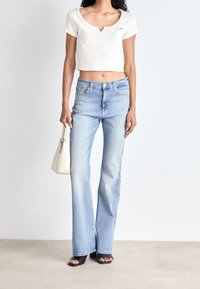 Biała krótka koszulka, jasnoniebieskie jeansy typu dzwony, czarne sandały na obcasie, oraz mała biała torebka. Gładka tekstura, swobodny fason.