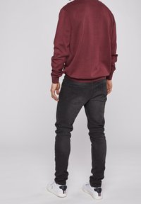 Burgundy sweater with a textured knit design, paired with fitted black jeans. Model wears white sneakers with dark accents.