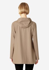 Chaqueta impermeable beige con capucha, mangas largas y detalles de botones a presión. Textura suave y mate, con un corte relajado.