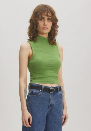 Green ribbed crop top with a high neck, paired with high-waisted blue denim jeans and a black belt. Minimalist design, fitted silhouette.