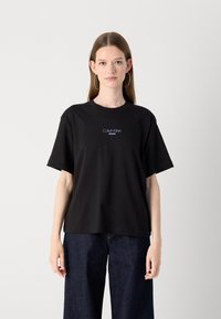 Black cotton t-shirt with a relaxed fit, featuring a blue logo “Calvin Klein JEANS” centered on the chest. Short sleeves, crew neck design.