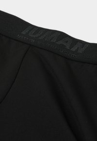 Schwarzer elastischer Bund mit dem eingeprägten Logo "HUMAN". Glatte, leichte Stoffqualität mit subtiler Textur und leichtem Faltenvergleich.