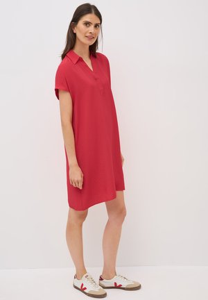 Vestido rojo de manga corta con cuello y tela texturizada, acompañado de zapatillas blancas con detalles en rojo y marrón.