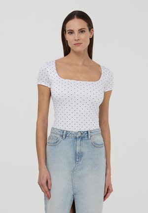 Body bianco a maniche corte con pois neri, scollatura quadrata e tessuto elasticizzato, abbinato a una gonna in denim blu chiaro con uno spacco.