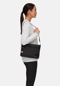 Schwarze Schultertasche aus glattem Stoff mit Klappenverschluss, verstellbarem Trageriemen und orangefarbener Akzentmarke. Verfügt über einen Reißverschluss und ein Logo-Patch.