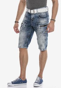 Denim shorts in lichtblauw met een vervaagde was, voorzien van rits- en patchzakken, gecombineerd met een witte geperforeerde riem en blauwe sneakers.
