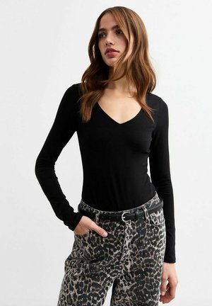 Zwart langesleeve bodysuit met een V-hals, gecombineerd met hoge taille jeans met luipaardprint en een zwarte riem. Gladde stofstructuur.