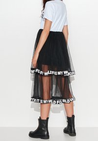 Czarna spódnica z tiulu z przezroczystą nakładką, z białym pasem u dołu z napisem. Zestawiona z jasnoniebieską bluzką i czarnymi bojowymi butami.