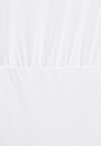 Tissu blanc avec couture horizontale et plis froncés au-dessus de la couture créant une légère texture et des plis.