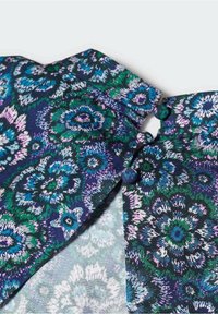 Látka s květinovým vzorem v odstínech modré, zelené a fialové, s rýhovaným límcem a zapínáním na knoflíky s kontrastní texturou.
