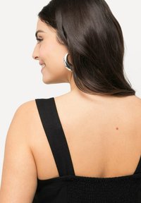 Musta hihaton toppi, jossa on rypytetty selkädesign. Ominaisuuksiin kuuluu paksut hihat ja sileä pinta, joka korostaa selän ja olkapäiden yksityiskohtia.