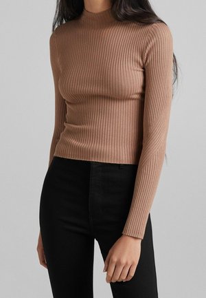 Haut brun à manches longues côtelé avec un col haut, présentant une silhouette ajustée et une texture douce ; associé à un pantalon noir ajusté.