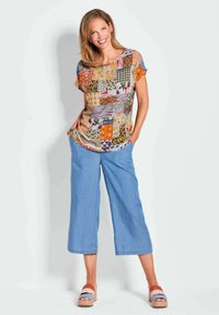 Multikleurige patchwork top met korte mouwen, losse pasvorm; gecombineerd met lichtblauwe wijd gesneden broek en multikleurige blokhak sandalen.