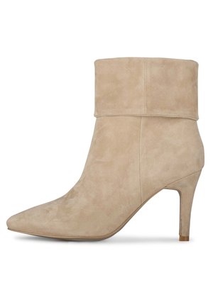Botte de cheville en daim beige avec un revers, un bout pointu et un talon fin. Texture lisse sans motifs visibles ni détails en métal.