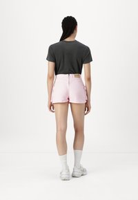 Vedere din spate a unei persoane îmbrăcate cu un tricou gri închis și pantaloni scurți roz deschis cu buzunare laterale. Sosete albe și adidași cu talpă groasă completează ținuta.