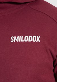 Sudadera burdeos con el logo blanco de "SMILODOX" en el frente. Tejido suave con una textura lisa y un diseño clásico con capucha.