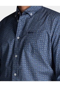 Blauwe button-up shirt met een klein, herhalend patroon van ovale vormen in wit en geel. Inclusief een borstzak en een button-down kraag.