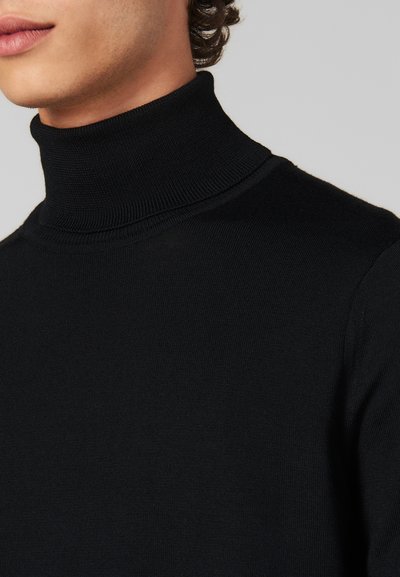 Maglione nero a collo alto con texture a coste. Vista ravvicinata che mette in evidenza il design senza cuciture e l'alta scollatura, su uno sfondo neutro.