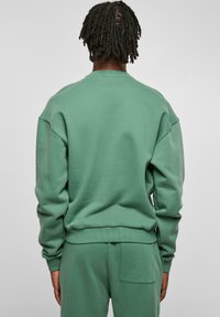 Sweat-shirt vert menthe avec une coupe décontractée, épaules tombantes, poignets côtelés avec une texture douce et un design minimaliste.