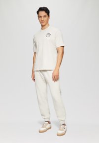 Lichtgekleurde katoenen t-shirt met korte mouwen en logodetail, gecombineerd met bijpassende katoenen joggingbroek. Gecompleteerd met crèmekleurige sneakers.