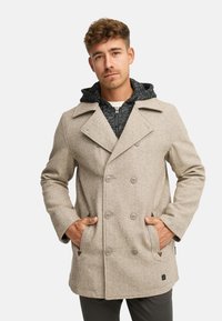 Cappotto doppiopetto beige in misto lana con grandi bottoni, tasche laterali e interno con cappuccio grigio. Tessuto liscio e vestibilità sartoriale.