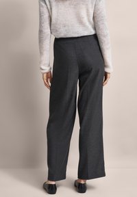 Graue weit geschnittene Hosen mit vertikalen Nähten und einer glatten Textur, kombiniert mit schwarzen Slippern und einem leichten, strukturierten Pullover.