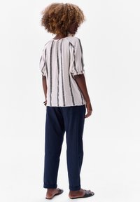 Lichte, gestructureerde blouse met zwarte verticale strepen, pofmouwen en ronde halslijn; gecombineerd met donkerblauwe, losse broek.