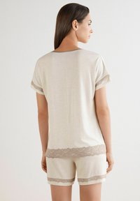 Conjunto corto de camiseta de manga corta y pantalones cortos en color beige claro, fabricado con un tejido suave, con un delicado encaje en las mangas y en el dobladillo, y un corte holgado.