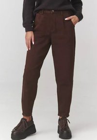 Brązowe spodnie w kolorze korduroy, zwężane, o wysokim stanie, z przednimi kieszeniami i zapięciem na guzik. Połącz z ciemnymi sneakersami dla kontrastu.