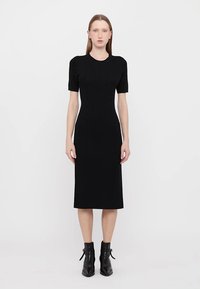 Black ribbed midi dress with short puff sleeves, fitted silhouette, round neckline, and smooth texture. Paired with ankle-height black boots.