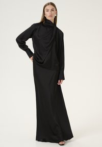 Sort satin langærmet top med draperet halsudskæring, parret med en matchende gulvlængde nederdel. Glat tekstur, minimalistisk design.