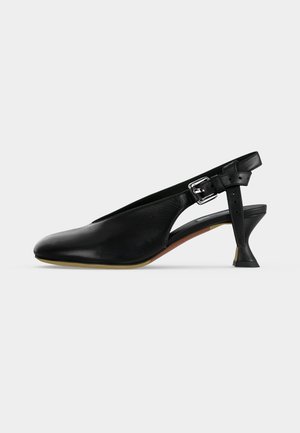 Sort læder slingback-sko med spids tå, sølvspænde på remmen og udvidet lille hæl på beige sål mod en ensfarvet baggrund.