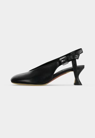 Μαύρο δερμάτινο παπούτσι slingback με μυτερή μύτη, λουράκι με ασημένια αγκράφα και φαρδύ χαμηλό τακούνι σε μπεζ σόλα, σε μονόχρωμο φόντο.
