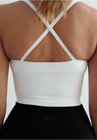 Hvid ribbet cropped tank top med justerbare krydsryg-stropper, parret med højtaljede sorte leggings. Diskret brandlogo nær kanten.