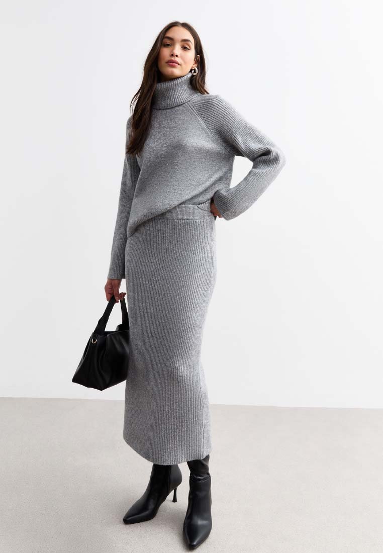 Szary prążkowany sweter z golfem i dopasowana długa spódnica, w połączeniu z czarnymi wysokimi botkami na obcasie i czarną torebką. Gładka faktura.