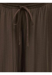 Pantalon en tissu marron avec taille à cordon, montrant un gros plan du nœud noué et de la taille élastique froncée.